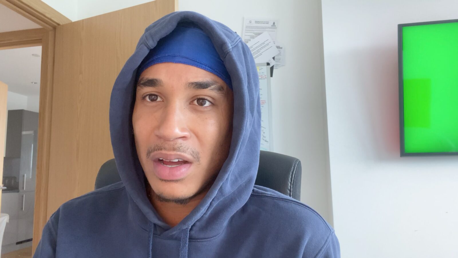 Joshua Arthur in a blue hoodie, vlogging in his room with a greenscreen on the wall